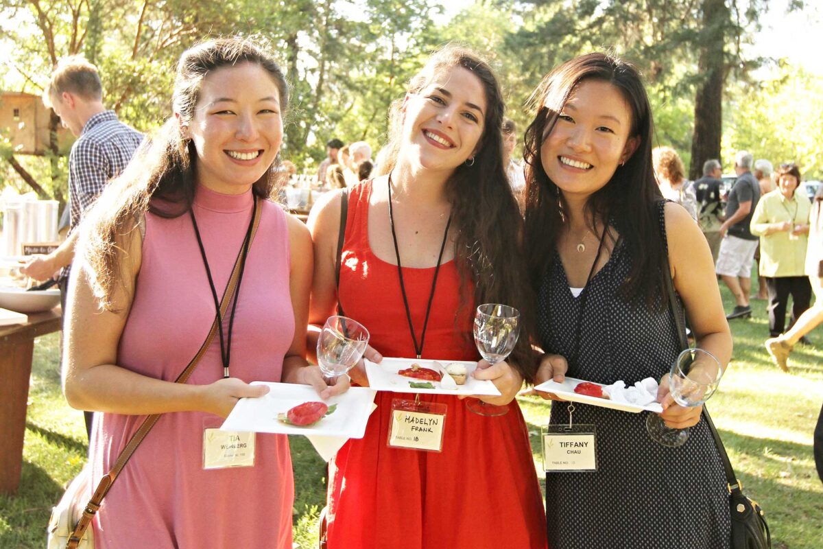 Three friends holding wine glasses smile at the annual Pure Mendocino fundraiser