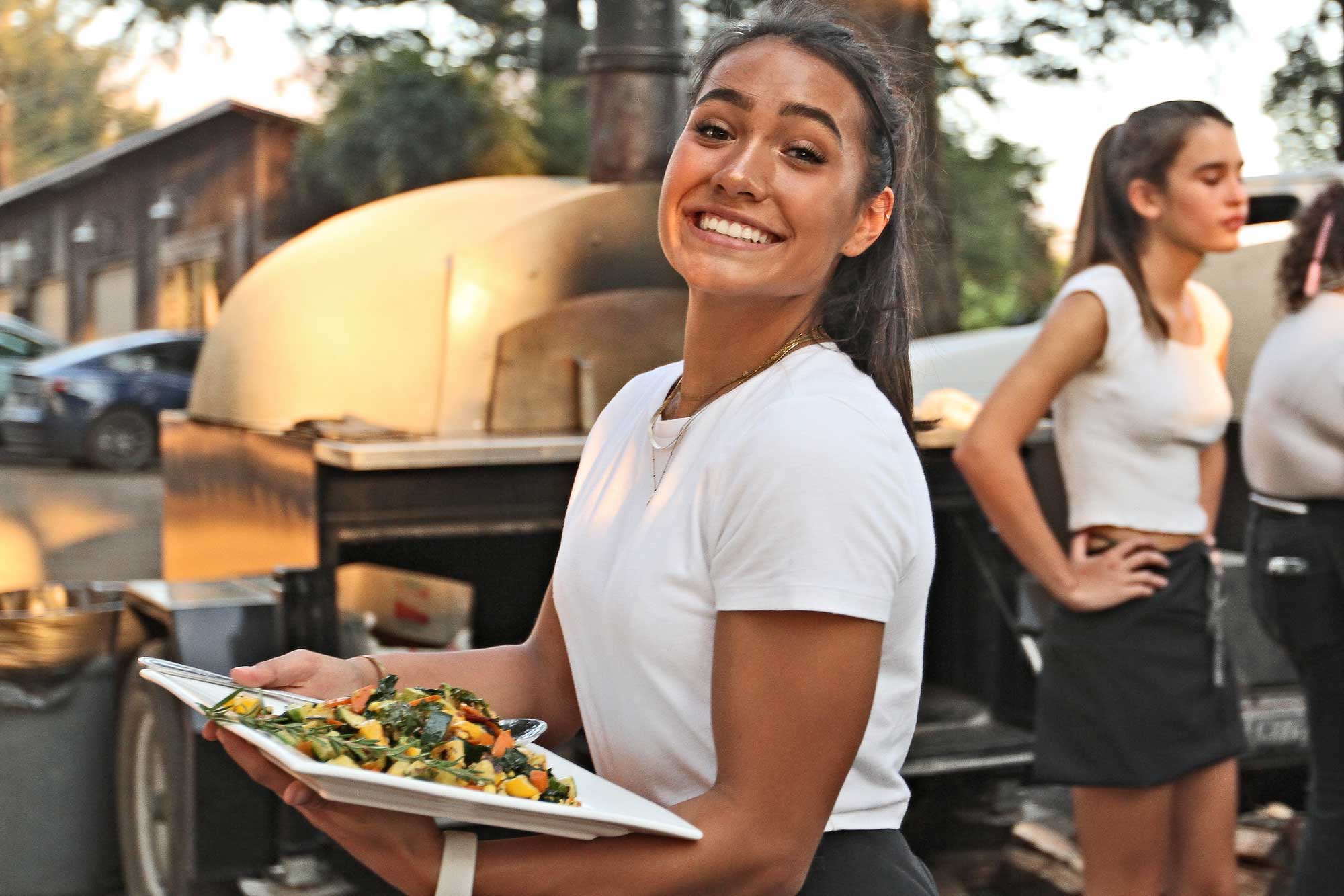 Smiling server carries plate of roast vegetables